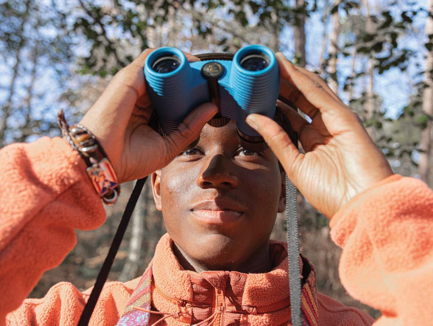 a young person faces the camera and raises binoculars