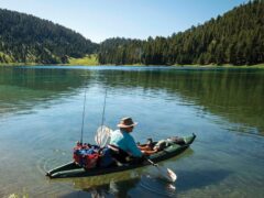 a person with fishing rods sits on a kayak in a pristine mountain lake